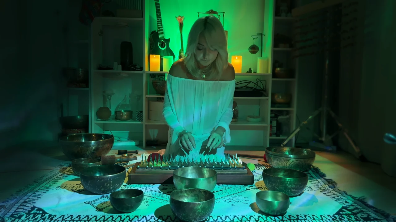 Viktoria playing the kalimba among Tibetan singing bowls in green light.