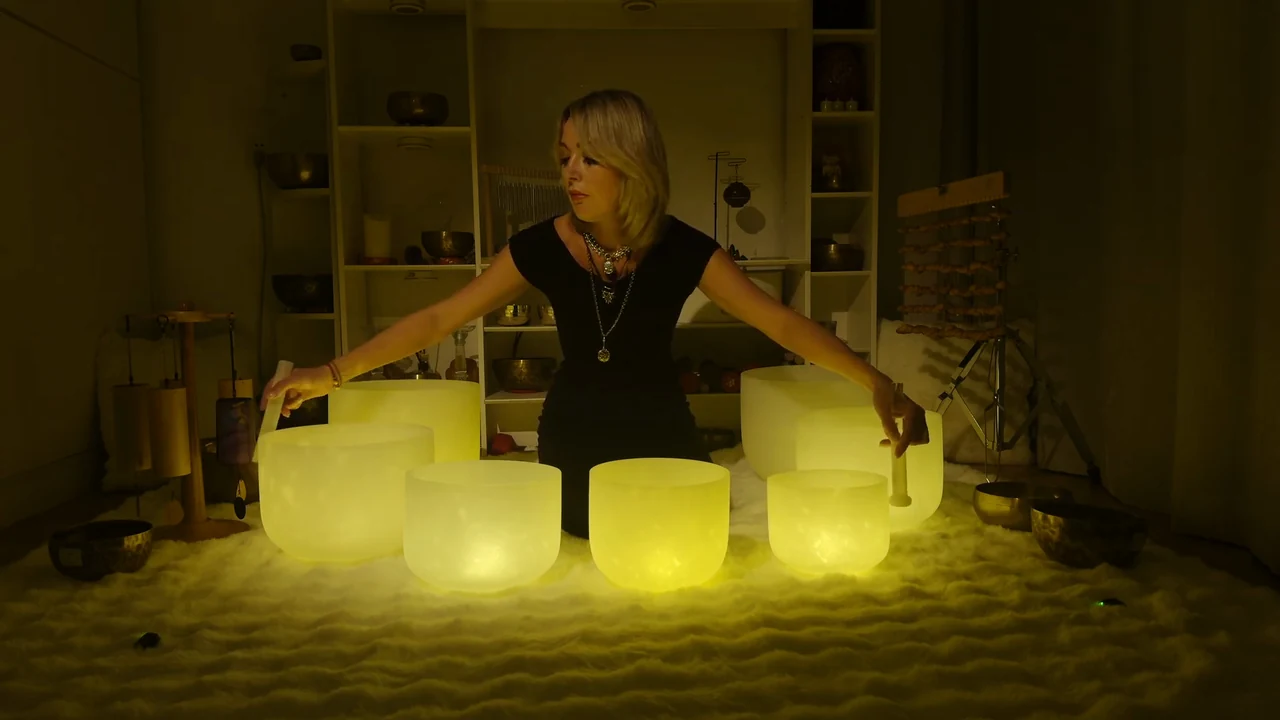 Viktoria with crystal and Tibetan singing bowls in a softly lit recording space.